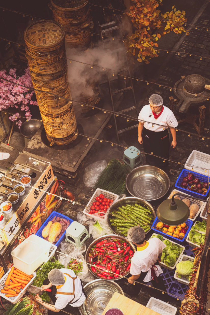 Fresh vegetables and cooks preparing food in a Chongqing community kitchen